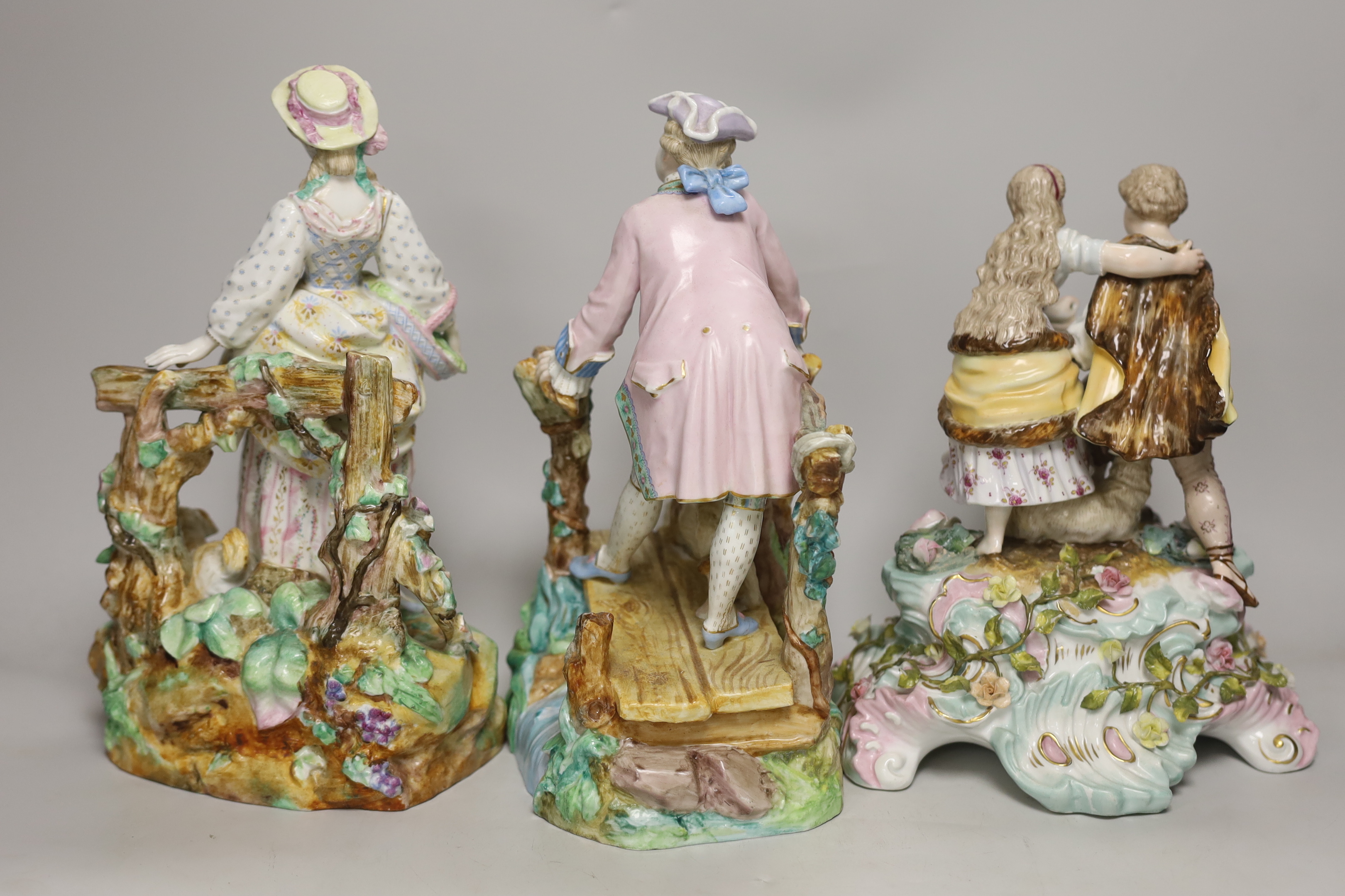 Three German porcelain figures including a Sitzendorf group of a young couple and a sheep, together with a pair of lovers with dogs, highest 28cm